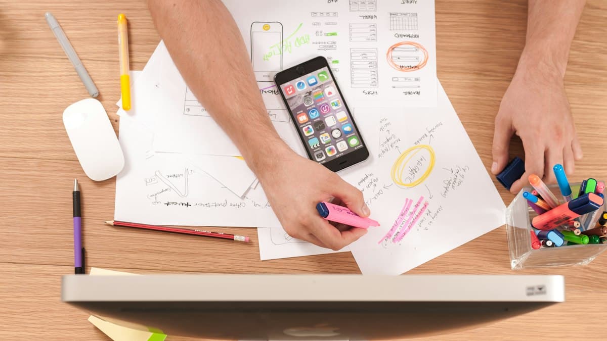 Top-down view of a desk with app wireframe sketches, a smartphone and highlighters